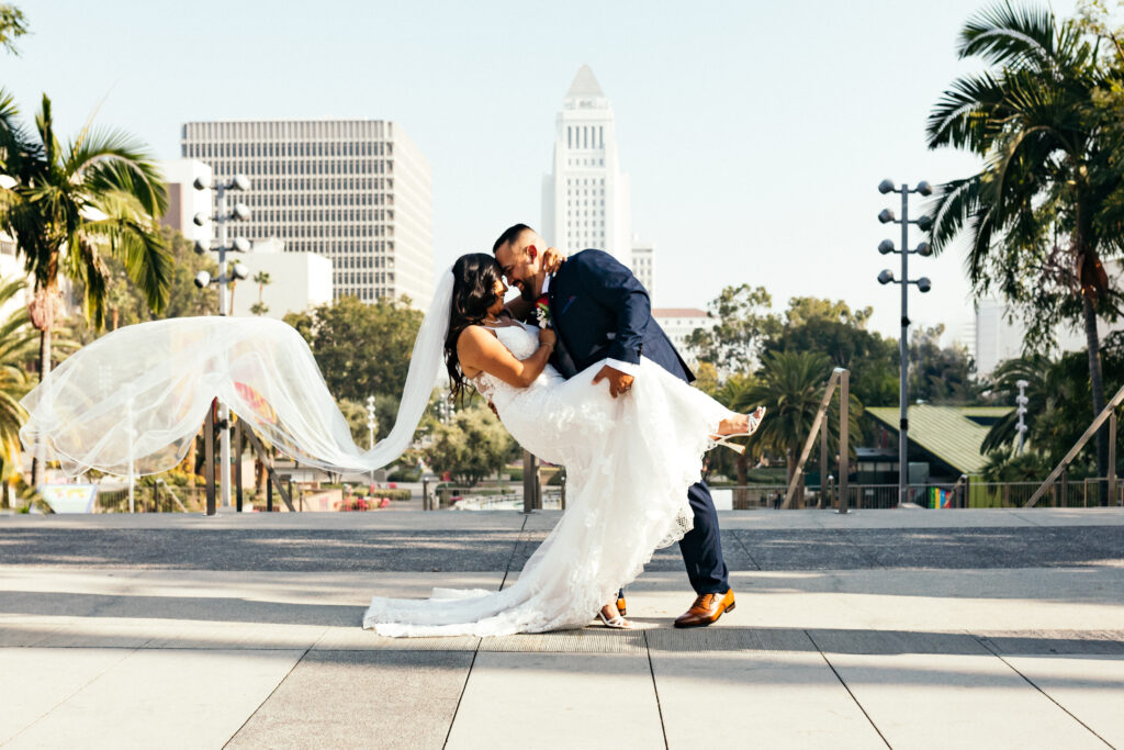 Bride and groom in front of LA City hall with the bride's veil flowing in the wind. Harrison Elder Photography- Turning your memories into art.